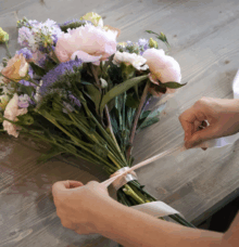 Händer som binder ett band runt en bukett med blandade blommor på ett träbord.